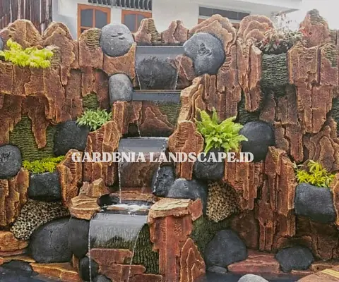 Air terjun dari susunan batu berbentuk tebing, dengan batu hitam bulat dan tanaman paku