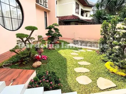 Taman rumput dengan batu pijakan pipih dan bonsai di samping rumah