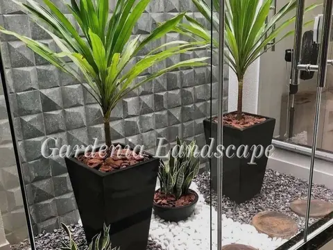 Taman mini di balik kaca dengan tanaman dalam pot hitam dan kerikil